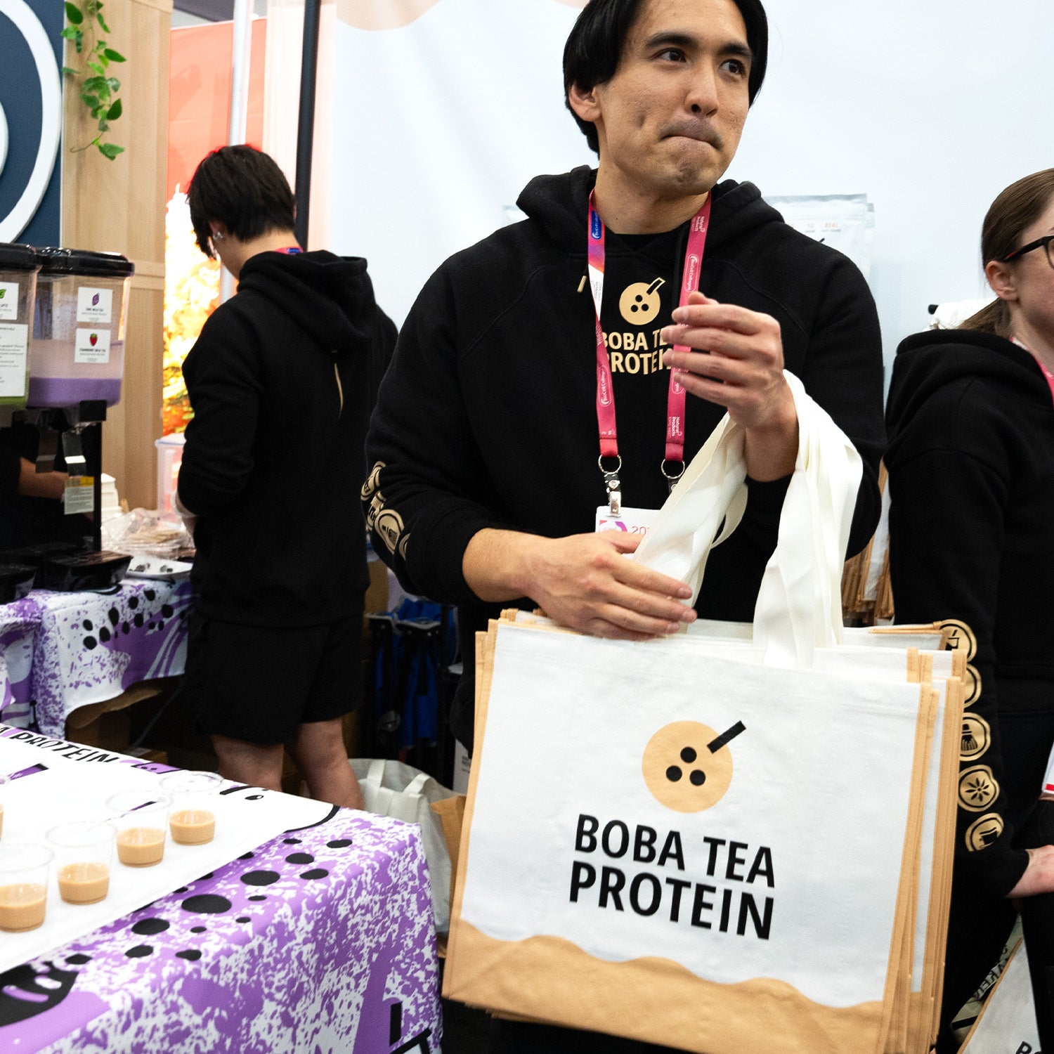 Person holding a tote bag with 'Boba Tea Protein' branding at an event.