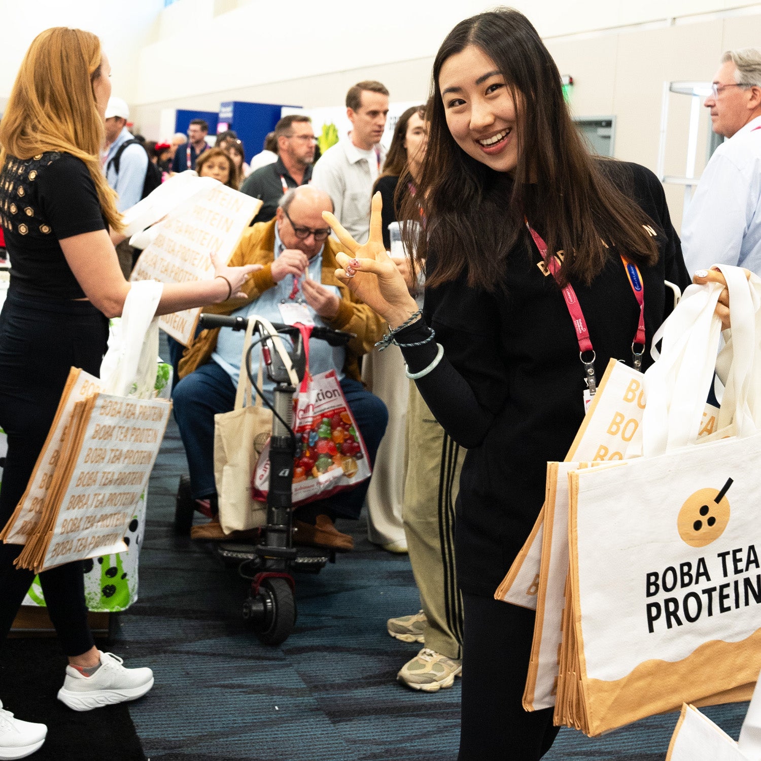 Woman holding a tote bag with 'Boba Tea Protein' text in a busy indoor setting