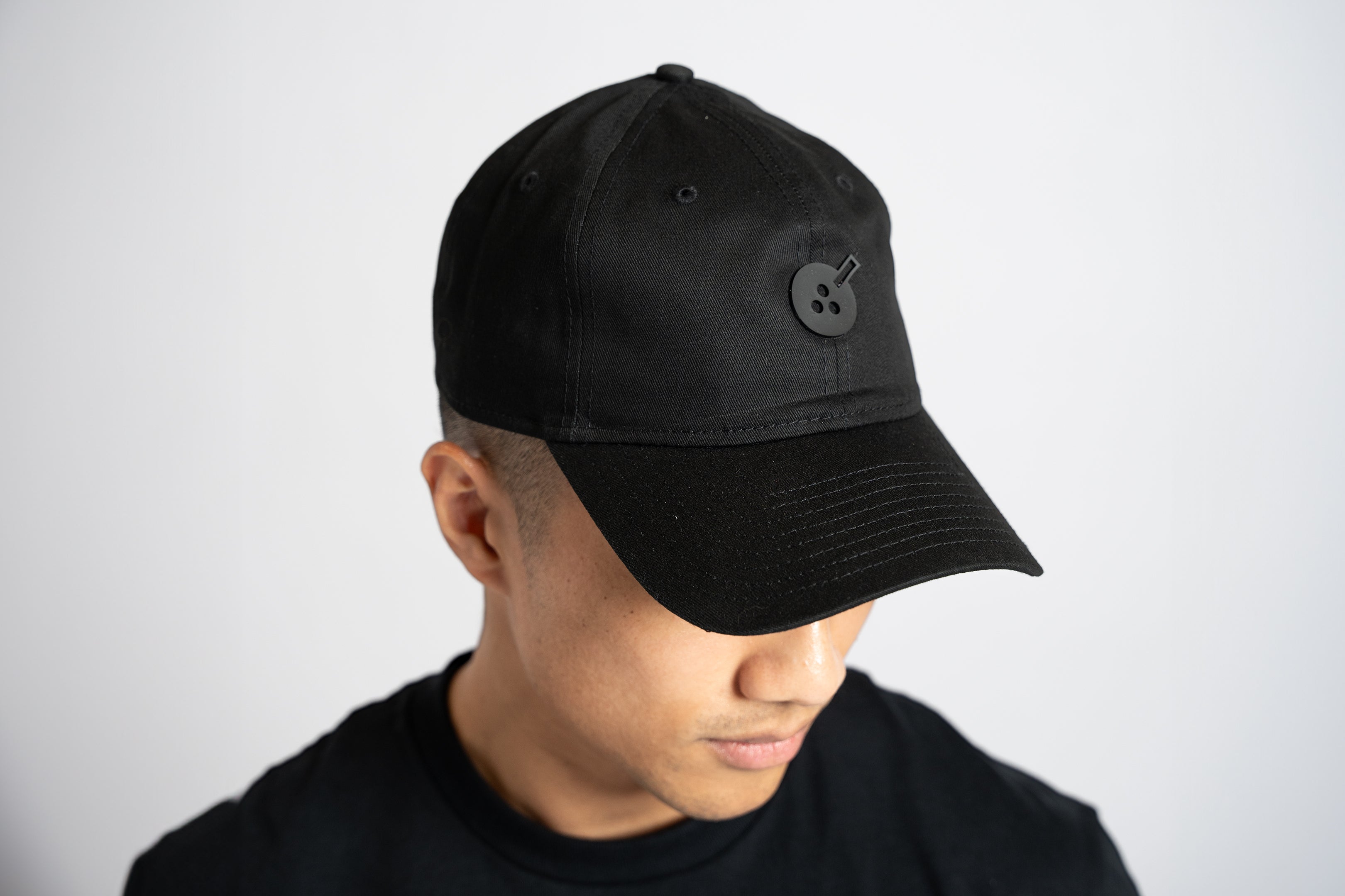 A black cloth hat in "dad hat" style, with a silicone embellishment in the same color in the shape of Boba Tea Protein's circular logo depicting a boba drink placed in the center of the front of the hat.