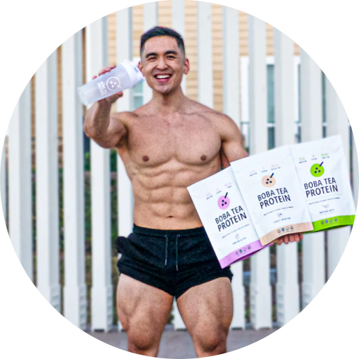 Shirtless man holding Boba Tea Protein shake and packs, smiling confidently outdoors.