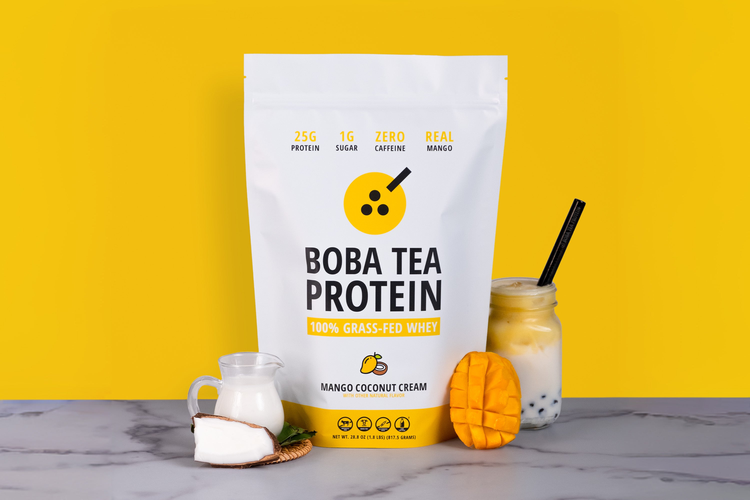 Boba Tea Protein package with a mango coconut cream flavor with mango, coconut, and a drink on a marble surface against a yellow background