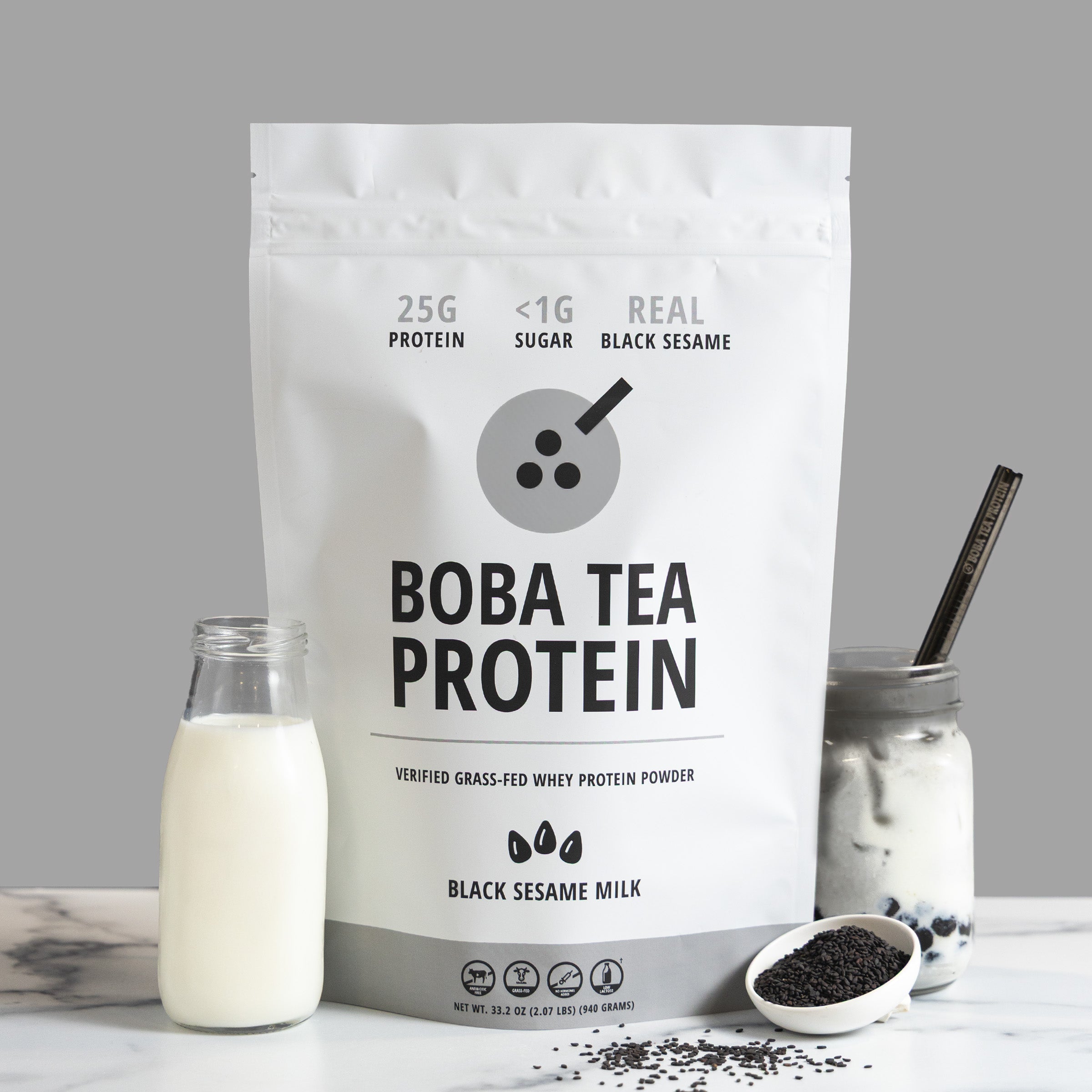 Boba tea protein package with a bottle of milk, black sesame seeds, and a Black Sesame Milk drink on a gray background