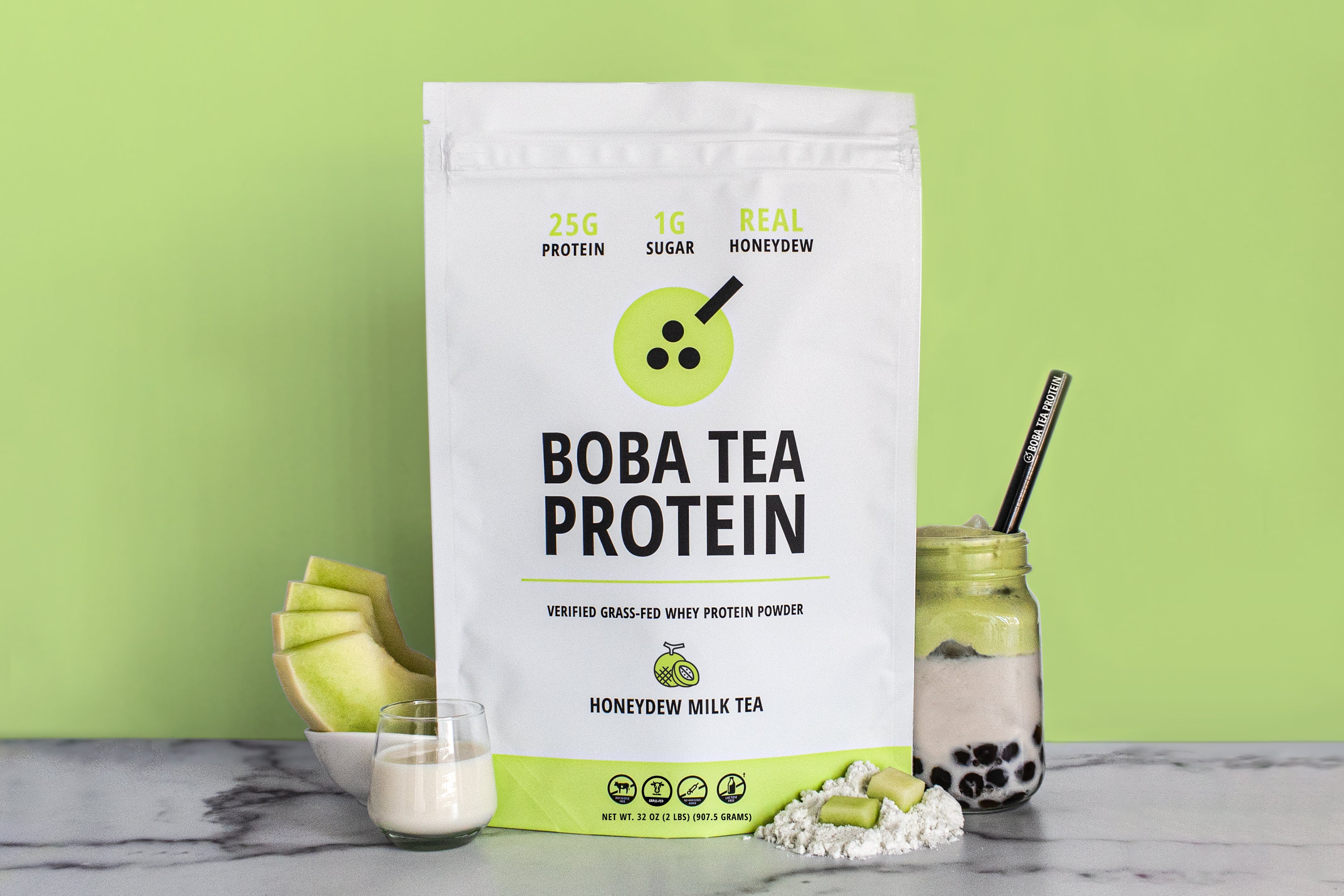 The image shows a bag of "Boba Tea Protein" powder in honeydew flavor, featuring highlights like "25g Protein" and "1g Sugar", against a background of bright light green matching the honeydew theme. In front are fresh honeydew slices, a glass of milk, a scoop of powder, and a jar of milk tea with tapioca pearls and a metal straw.