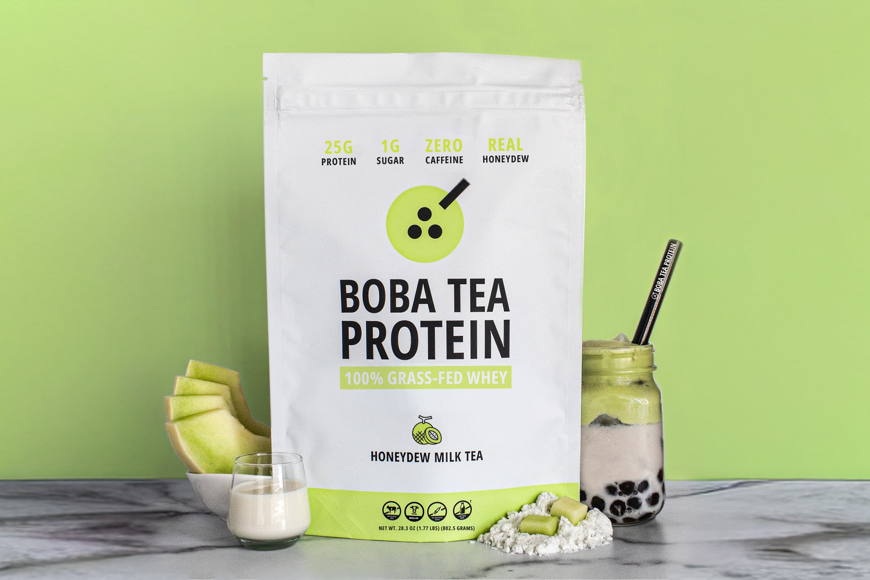 The image shows a bag of "Boba Tea Protein" powder in honeydew flavor, featuring highlights like "25g Protein" and "1g Sugar", against a background of bright light green matching the honeydew theme. In front are fresh honeydew slices, a glass of milk, a scoop of powder, and a jar of milk tea with tapioca pearls and a metal straw.