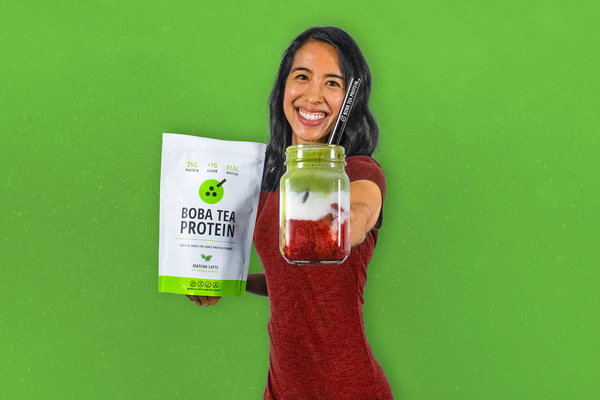 Woman holding a package of Matcha Latte Boba Tea Protein and a jar of a Matcha Latte with strawberry compote against a green background