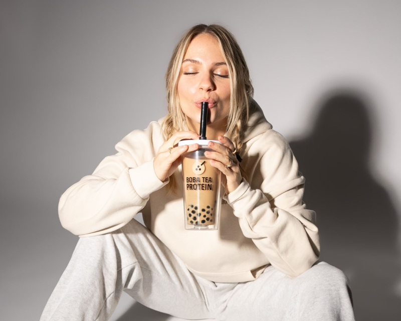 Woman in loungewear sipping Boba Tea Protein with eyes closed, enjoying the drink