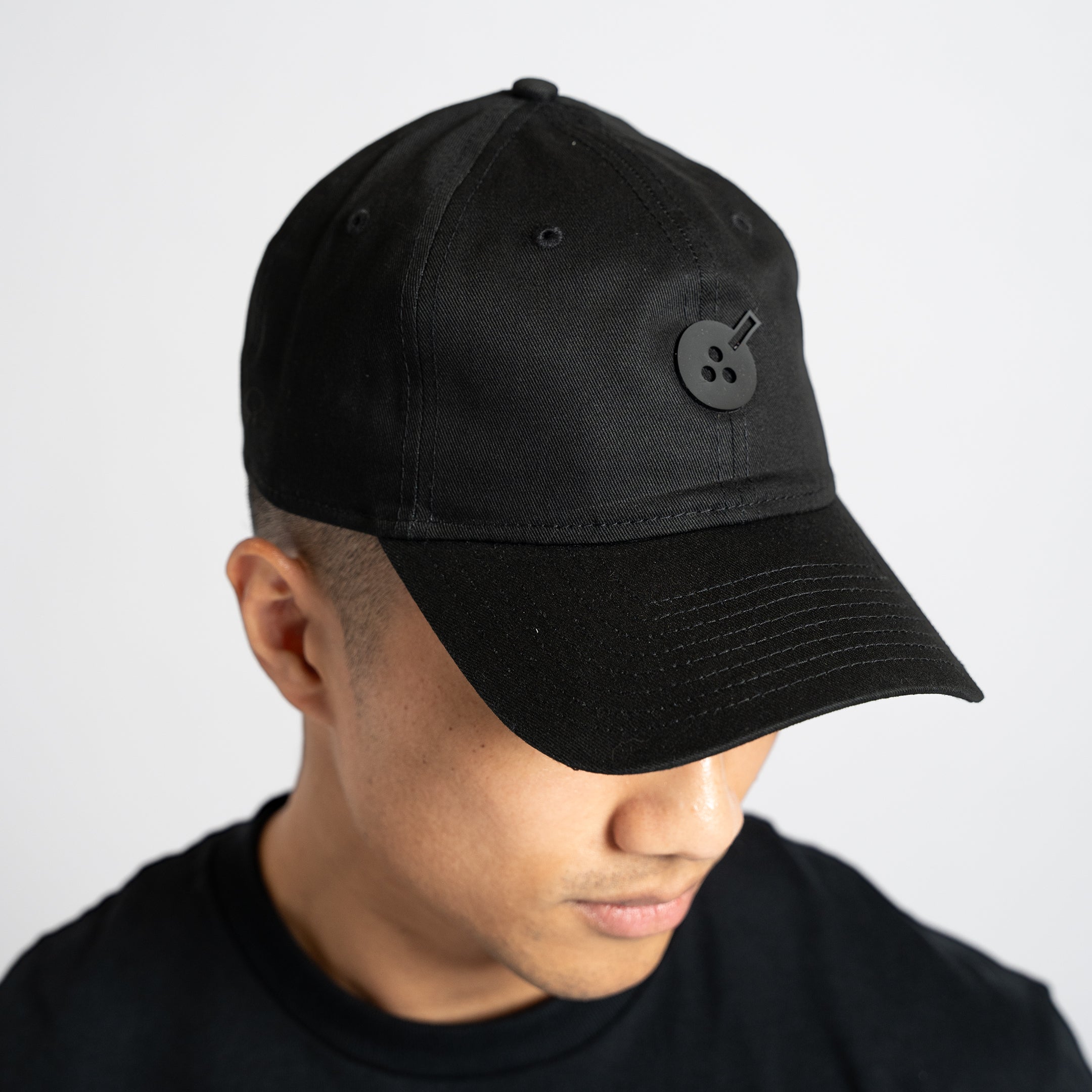 A black cloth hat in "dad hat" style, with a silicone embellishment in the same color in the shape of Boba Tea Protein's circular logo depicting a boba drink placed in the center of the front of the hat.