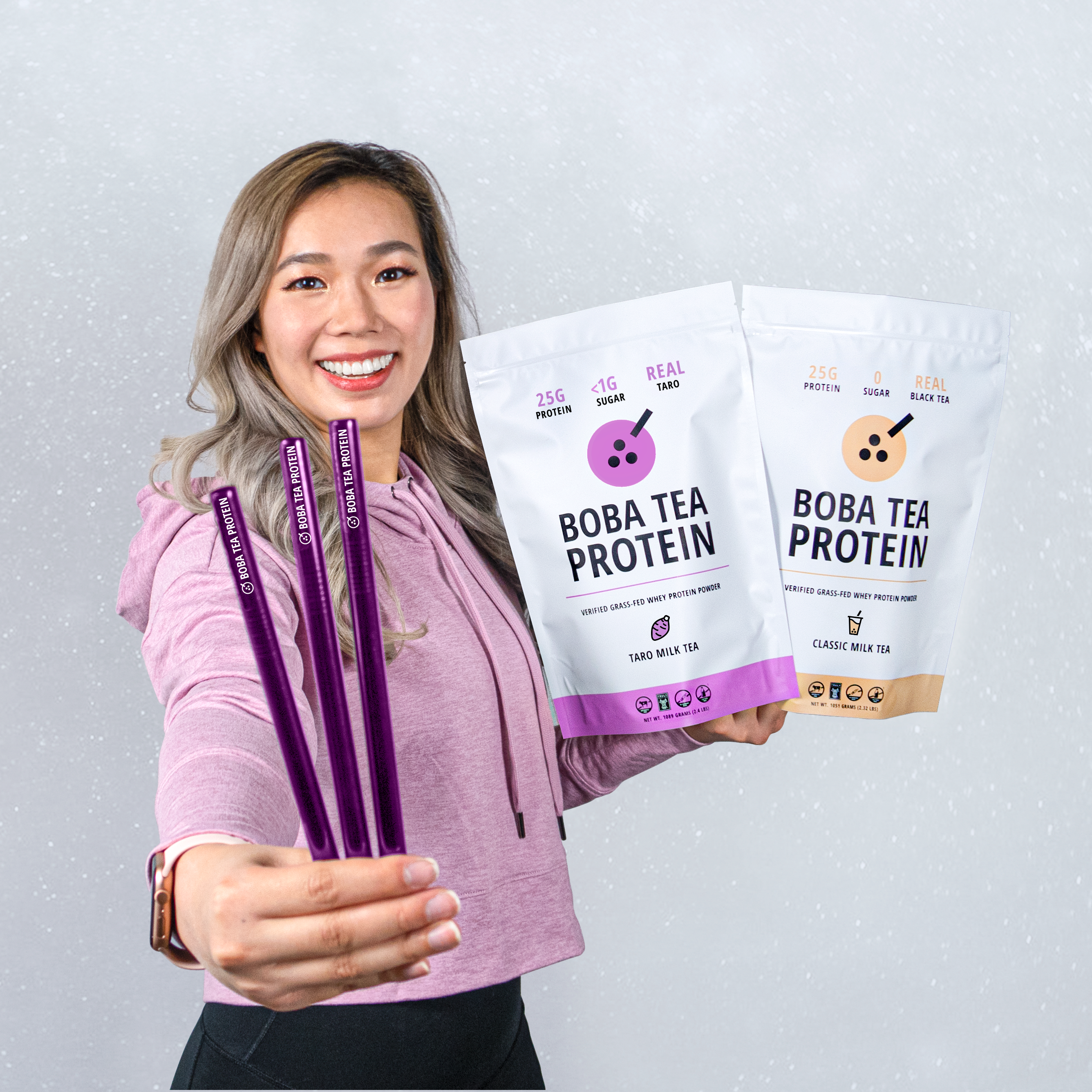Woman holding Boba Tea Protein packages and straws against a light gray background