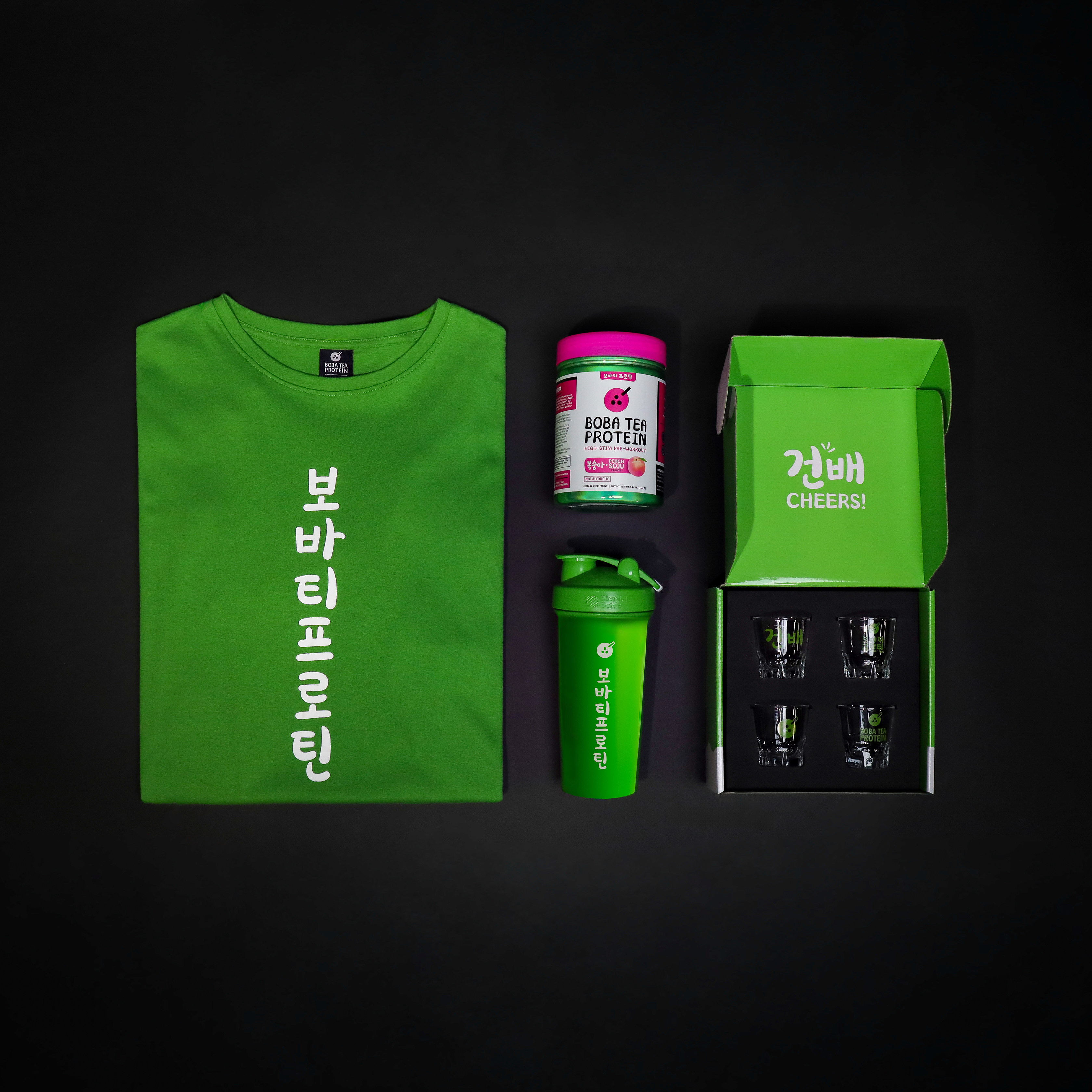 Green t-shirt, pre-workout supplement, shaker bottle, and box of glass shot cups on a black background
