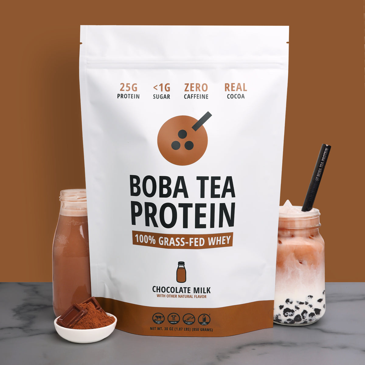 A 25-serving stand-up pouch of Boba Tea Protein Chocolate Milk whey powder stands on a gray marble surface against a solid brown background. The white and brown packaging features a milk bottle graphic and text indicating 25g protein, <1g sugar, zero caffeine, and real cocoa.