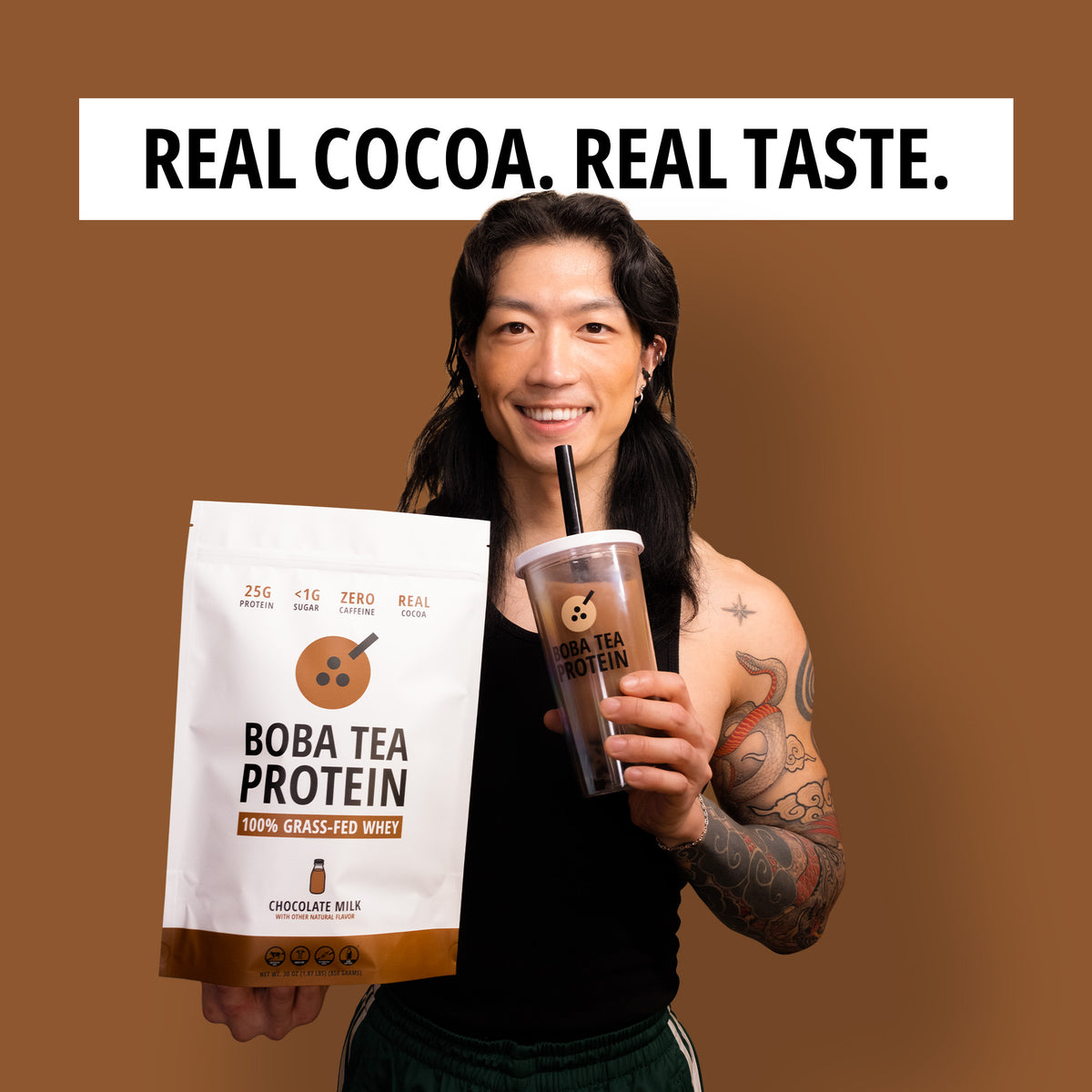 A smiling man holds a large white bag of Boba Tea Protein and a clear plastic cup filled with chocolate protein and tapioca pearls, set against a solid brown background with the text 'REAL COCOA. REAL TASTE.'