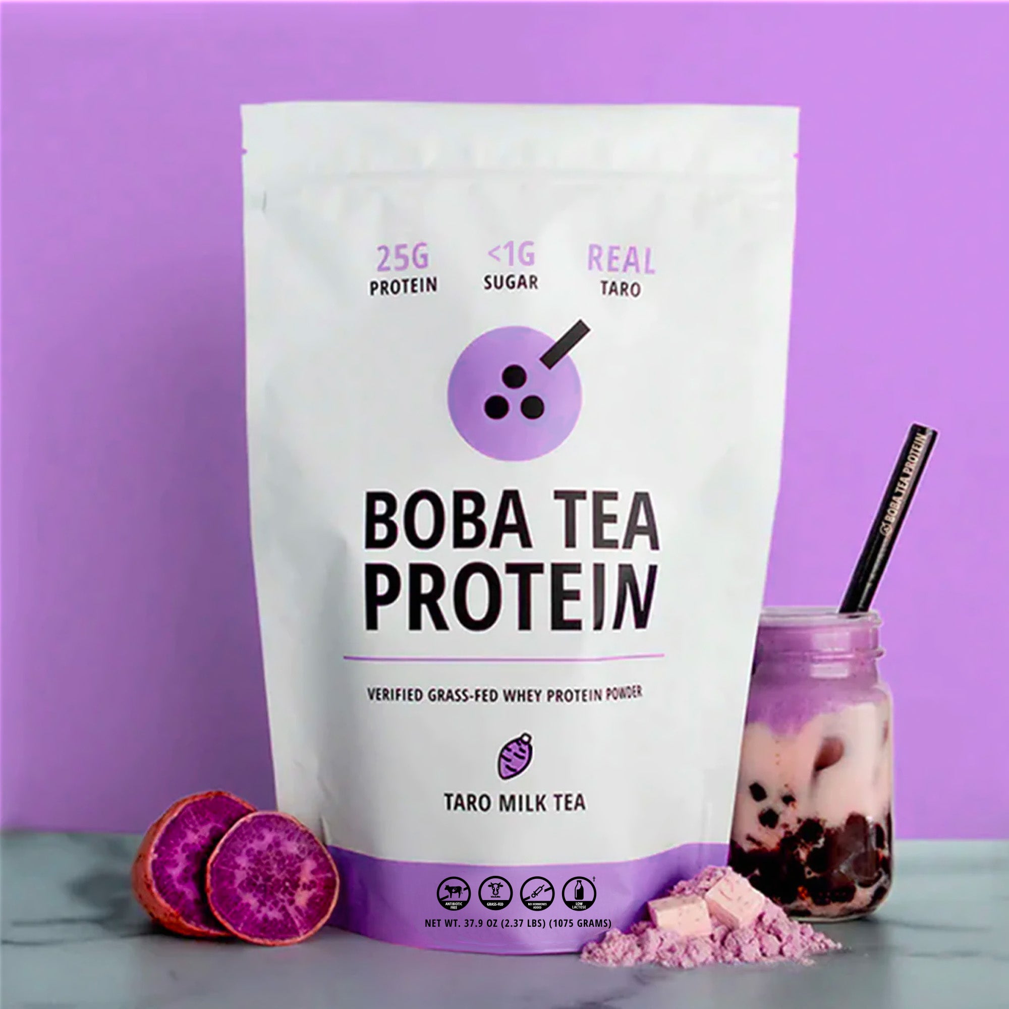 Bag of boba tea protein powder with a glass of milk tea and taro root on a purple background